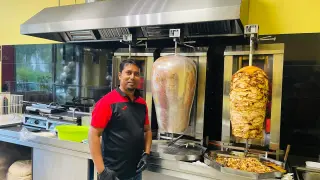 Mężczyzna w kuchni z dwoma obrotowymi rożnami z mięsem. Obok niego stos placków do kebaba. To właśnie kraftowe mięso kebab, co to znaczy? To świeżość i smak!
