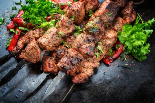 Chilli kebab na grillu, soczyste kawałki mięsa z przyprawami, podane z papryczkami i natką pietruszki.